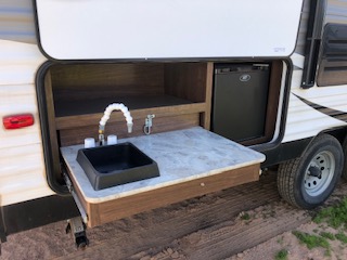 RVs parked in an open space, with one RV featuring a side opening that includes a washing sink