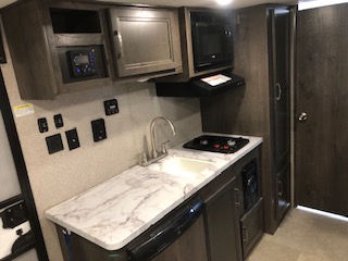 Travel trailer equipped with a gas cooking area, including other kitchen items, showcasing its functional kitchen space